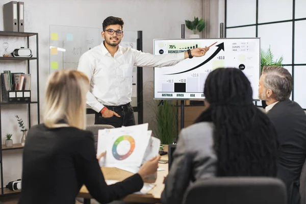 Orta yaşlı erkek sakallı Hintli şef dijital duvar ekranında şirketlerin çalışma bilgilerini gösteriyor.