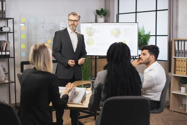 Çok ırklı yatırımcılar, yakışıklı orta yaşlı erkek menajer masada otururken...
