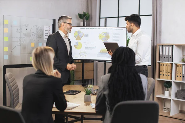 Karışık ırk iş adamlarından oluşan bir ekip orta yaşlı erkek sakallı şeflerini dinliyor.