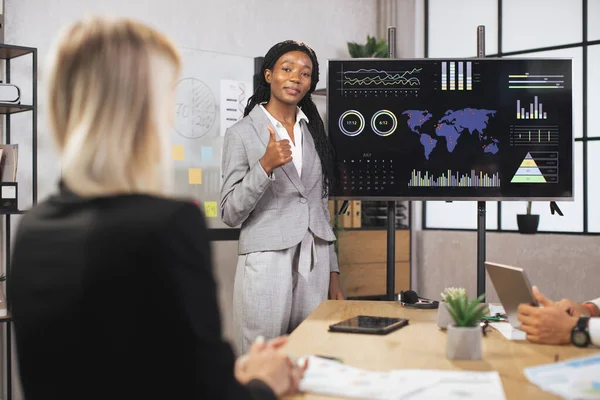 Çekici pozitif gülümsemeli başarılı genç iş kadını, şirketlerin çalışma bilgilerini gösteriyor