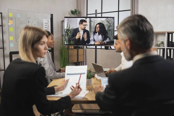Tým různých podnikatelů se dívá na obrazovku během videokonference v kanceláři — Stock fotografie