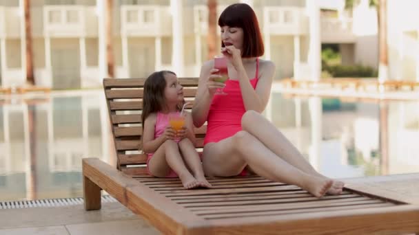 Mom with cocktail glass and her daughter with orange juice lying on a wooden deck chair. — Stock Video