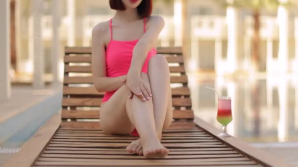 Jeune femme caucasienne en bikini rose élégant avec verre à cocktail sur chaise longue en bois. — Video