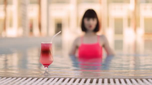 Woman in bright pink swimsuit, in resort swimming pool drinking refreshing colorful cocktail — Stock Video