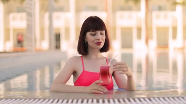 Femme en maillot de bain rose vif, dans la piscine de villégiature boire cocktail coloré rafraîchissant — Video