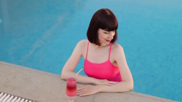 Femme en maillot de bain rose vif, dans la piscine de villégiature boire cocktail coloré rafraîchissant — Video