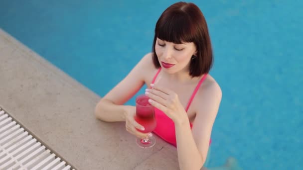 핑크 색 수영복을 입은 여성 이 맑은 여름날 칵테일을 마시며 호화 리조트 수영장에서 수영을 즐기고 있다 — 비디오