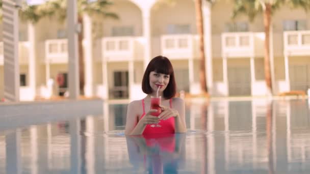 身穿粉色泳衣的白人妇女，在游泳池里喝鸡尾酒放松一下 — 图库视频影像
