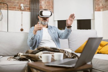 Kanepede VR kulaklıklarıyla eğlenen olgun bir adam.