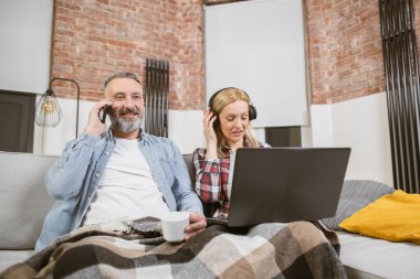 Kadın dizüstü bilgisayar kullanırken, yetişkin bir erkek cep telefonuyla konuşuyor.