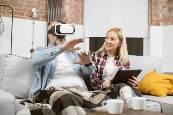 Férfi ül a kanapén VR headset, miközben a nő használja tabletta — Stock Fotó