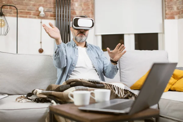 Homme d'âge moyen assis sur le canapé dans le casque VR et gestuelle — Photo