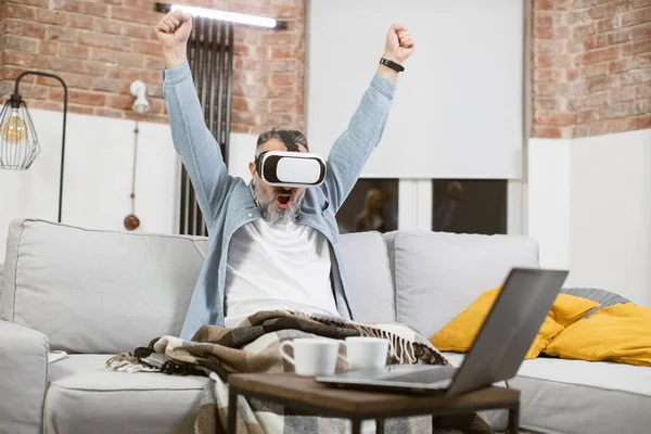 VR kulaklıkla koltukta el kol hareketi yapan heyecanlı bir olgun adam.