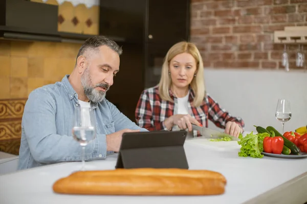 Woman chopping vegetables while man using tablet in kitchen — Stock Fotó