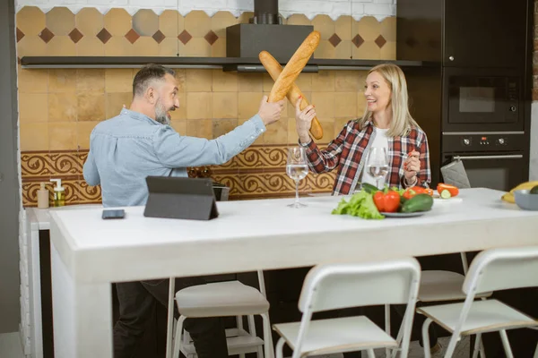 Couple using baguettes for playful fight on bright kitchen — Stock Fotó