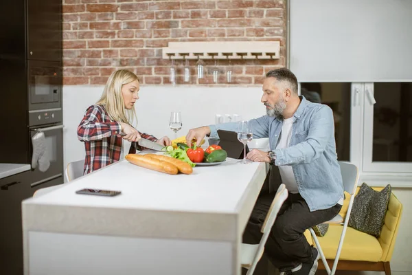 Mature woman cutting vegetables while man using tablet — Stock Fotó