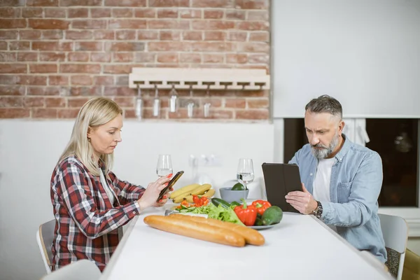 Married couple using tablet and smartphone on kitchen — стоковое фото