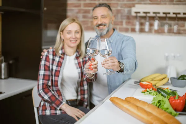 Mature couple making toast with glasses of water on kitchen — Stock Fotó