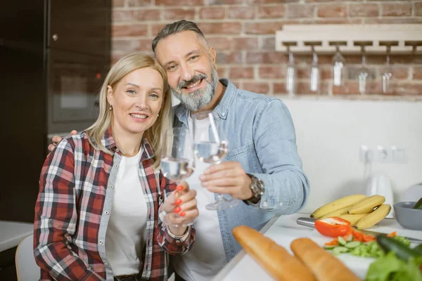 Mature couple making toast with glasses of water on kitchen — Stock Fotó