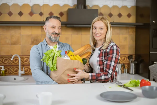 Mature married couple unpacking grocery bag on kitchen — стоковое фото