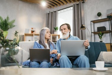 Sevimli yaşlı aile kanepeye dizüstü bilgisayar kullanarak oturur..