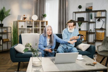 Mutlu, olgun bir aile evde bilgisayar oyunu oynuyor, kanepede dizüstü bilgisayarla oturuyor ve joystick kullanıyor..