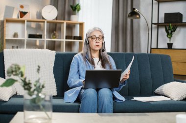 Evdeki oturma odasında video sohbet için kulaklık ve dizüstü bilgisayar kullanan güzel bir kadın..