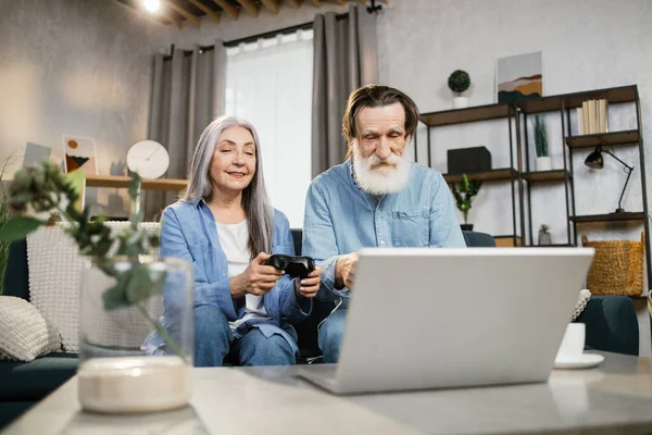 Πορτρέτο της όμορφης ώριμης γυναίκας και του γενειοφόρου συζύγου της που κάθεται στον καναπέ και παίζει βιντεοπαιχνίδια — Φωτογραφία Αρχείου