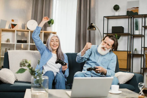 Szczęśliwy starszy biały para siedzi na kanapie z bezprzewodowy joysticks w ręce — Zdjęcie stockowe