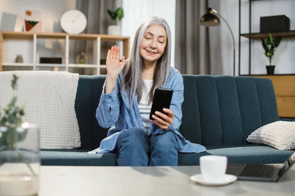 Χαμογελώντας ελκυστική γκρίζα μαλλιά γυναίκα χρησιμοποιώντας smartphone στο σπίτι, πληκτρολογώντας μήνυμα ή διαβάζοντας ειδήσεις — Φωτογραφία Αρχείου