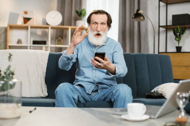 Gri sakallı, mutlu duygusal yüzlü ve iyi haberler aldıktan sonra yumruğunu kaldıran emekli.