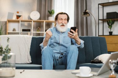 Gri sakallı, mutlu duygusal yüzlü ve iyi haberler aldıktan sonra yumruğunu kaldıran emekli.