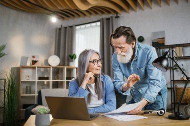 Sevgili yaşlı adam ve kadın aydınlık ofiste otururken mali raporları analiz ediyorlar..