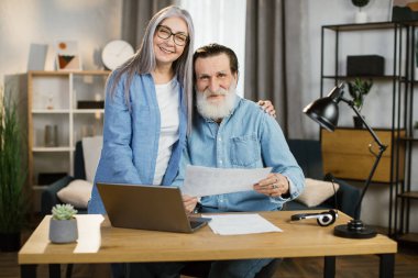 Gülümseyen olgun beyaz kadın ve erkek ofiste çalışmak için modern dizüstü bilgisayar kullanıyor.