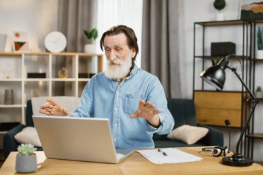 Uzaktan görüntülü konuşma için modern laptop kullanan gülümseyen olgun iş adamı.