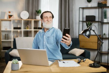 Gülümseyen olgun iş adamı modern akıllı telefon kullanarak özçekim fotoğrafları çekiyor..