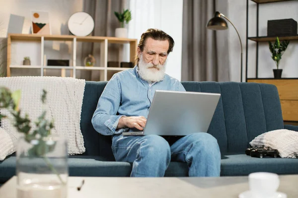 Όμορφος ώριμος κύριος χρησιμοποιώντας το laptop για συνομιλία βίντεο κάθεται στον καναπέ στο σαλόνι στο σπίτι — Φωτογραφία Αρχείου