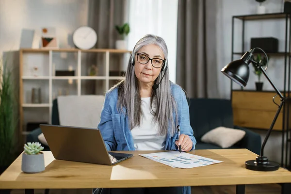 Attractive caucasian grey-haired woman sitting at desk and typing on laptop. — Stock Photo, Image