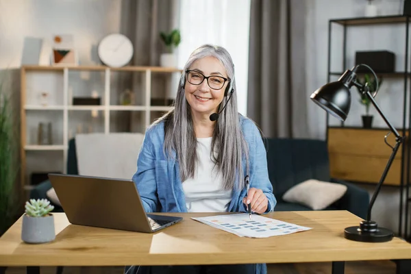 Attractive caucasian grey-haired woman sitting at desk and typing on laptop. — Stock Photo, Image
