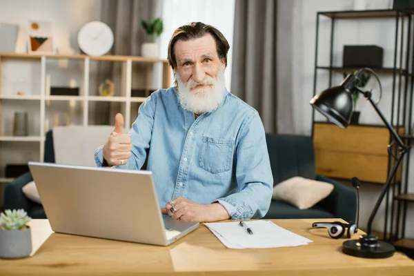 Guapo desarrollador de software senior en ropa casual escribiendo en el ordenador portátil mientras está sentado en el lugar de trabajo —  Fotos de Stock