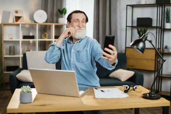 Modern akıllı telefondan video çağrısında gülümseyen ve el kol hareketi yapan mutlu genç bir adam.