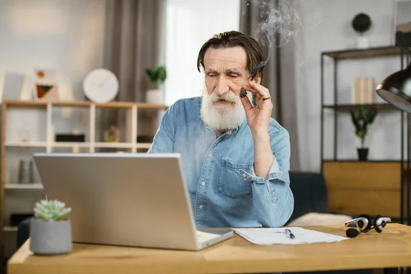 Πορτρέτο του όμορφος κομψό ώριμος επιχειρηματίας με πούρο κάθεται στο γραφείο με φορητό υπολογιστή — Φωτογραφία Αρχείου