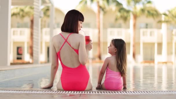 Happy family in the pool, having fun, mom giving to drink orange juice to her daughter — Stockvideo
