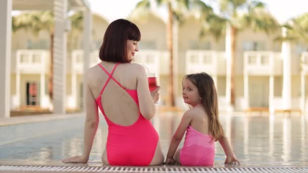Back view of happy caucasian mother drinking a cocktail and her daughter look at each other — Stockvideo