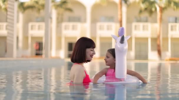 Mom plays with her little cute daughter with unicorn inflatable ring in the pool. — Vídeo de stock