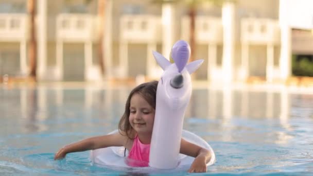 Child in swimming pool on unicorn inflatable violet ring. — Vídeo de Stock