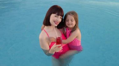 Küçük tatlı güzel kız, annesini turkuaz suyla egzotik bir havuzda kucaklıyor..