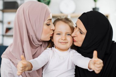 Müslüman bir kız ve mutlu bir büyükanne torununu yanaklarından öpüyor.