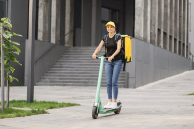 Teslimat, sırt çantalı kadın şehir caddesinde scooter sürüyor..