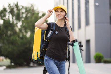 Şehirde elektrikli scooterla dururken akıllı telefon kullanan teslimatçı kadın..